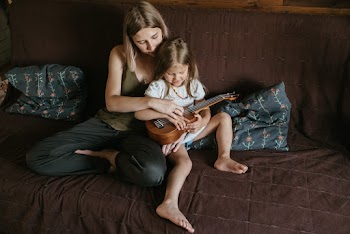 Woman in Grey Sleeveless Top With Girl on Her Lap Playing Ukulele