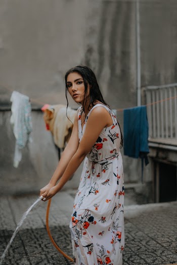 Woman in Long Floral Dress Holding Hose Pipe