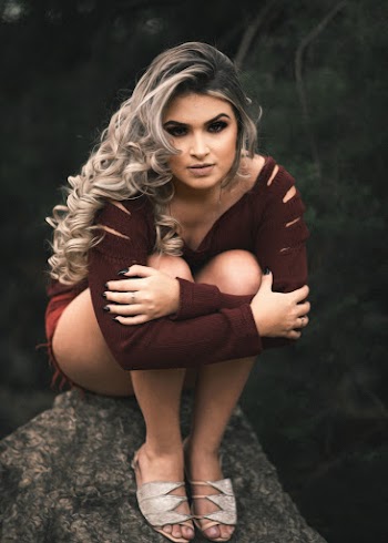 Woman in Maroon Long-sleeved Top Sitting on Rock While Holding Both Legs