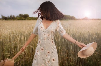 Woman in Multicolored Floral Dress Standing in Middle of Crop Field Holding Straw Hat