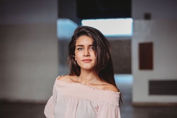 woman in nude off-shoulder shirt standing beside concrete wall selective focus photography