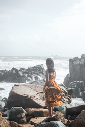 Woman in Orange Dress Standing on Rock Groynes