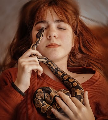 Woman in Orange Knit Sweater Holding Brown and Black Snake
