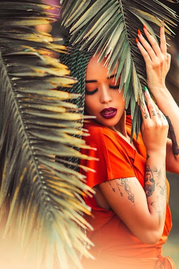 Woman in Orange Shirt Standing Under Coconut Palm Fronds
