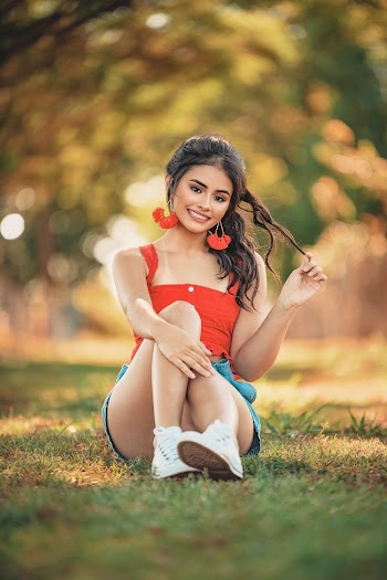 Woman in Orange Tank Top and White Shorts Sitting on Green Grass