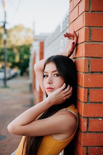 Woman in Orange Tank Top Leaning on Red Brick Wall