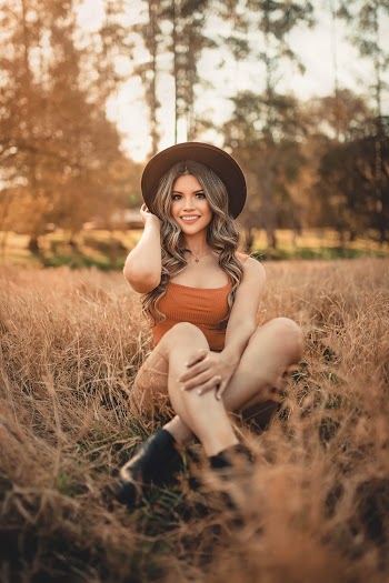 Woman In Orange Top Sitting In A Grass Field