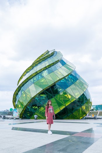 Woman in Pink Long-sleeved Midi Dress Standing Near Green and Blue Landmark Under Gray and White Sunny Cloudy Sky during