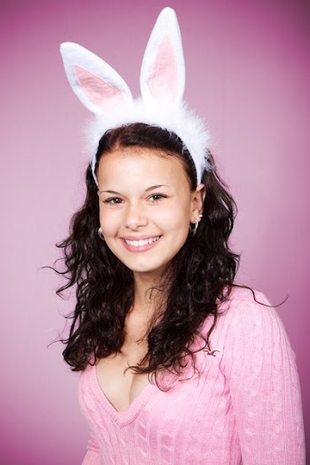Woman in Pink Sweater Wearing Bunny Headband Smiling Against Pink Background