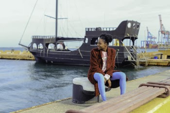 Woman in Red Cardigan Sitting on Black Metal Near Boats