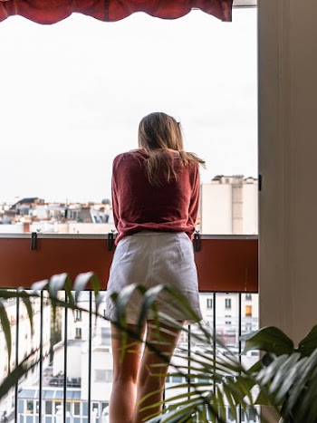 Woman in Red Dress Shirt and White Shorts Looking Out of Balcony
