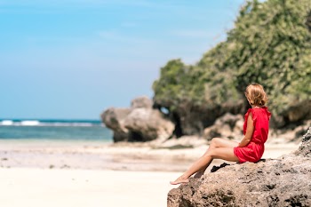 Woman in Red Dress Sitting on Brown Rock