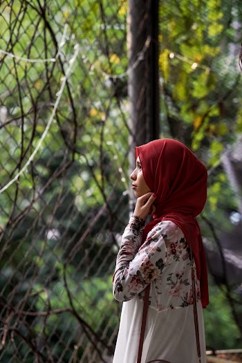 Woman in Red Headscarf Standing Near Chain-link Fence