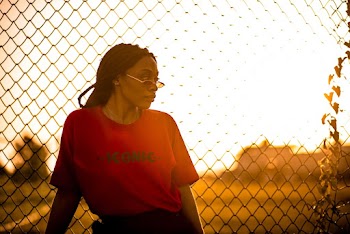 Woman in Red Konic Crew Neck T-shirt Standing in Front of Wire Mesh Fence