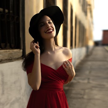 Woman in Red Off-shoulder Dress Holding Black Sun Hat While Looking Above and Closing Eyes