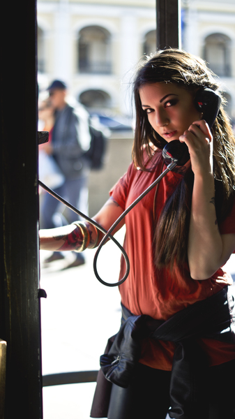 Woman in Red T-shirt Holding Telephone Inside Telephone Booth