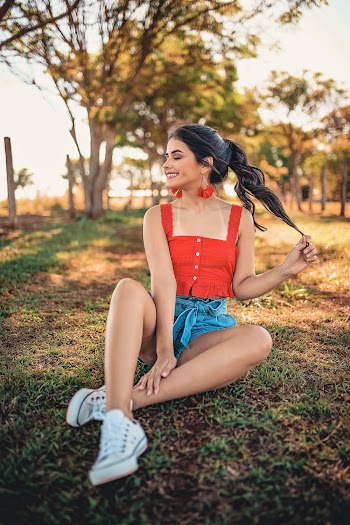 Woman in Red Tank Top and Blue Denim Shorts Sitting on Green Grass
