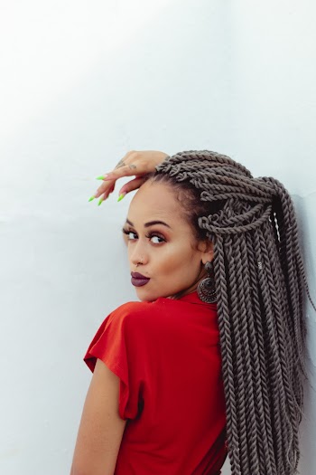 Woman In Red Top With Braided Hair Leaning On White Wall