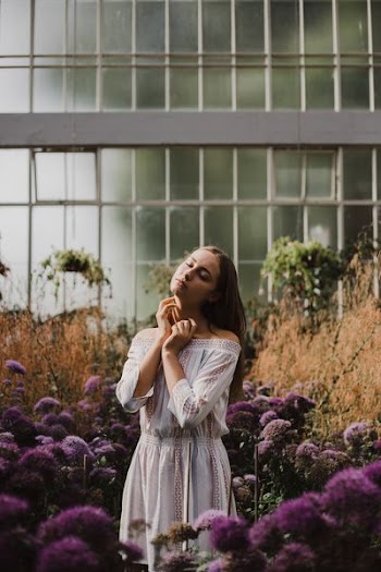 woman in standing in between purple petaled flower inside green house