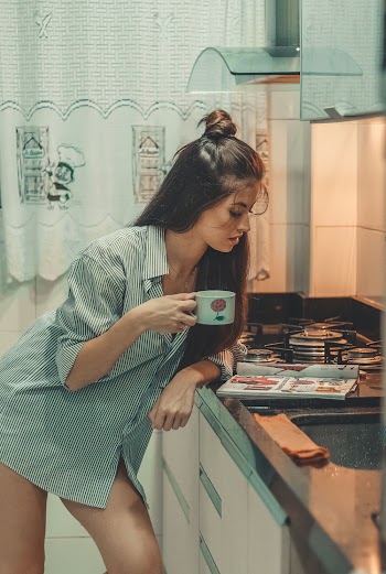 Woman in White and Grey Stripe Holding Mug Leaning on Kitchen Table