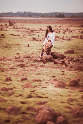 Woman in White Cardigan and Brown Pants Sitting on Stump during Daytime