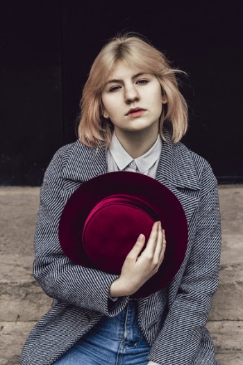 Woman in White Collared Top and Gray Coat Holding Red Fedora