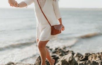 woman in white dress and brown leather sling bag walking on cliff