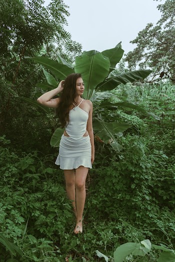 Woman in White Haltered Top With Mini Skirt Walking on Grass Field While Holding Head Using Right Hand