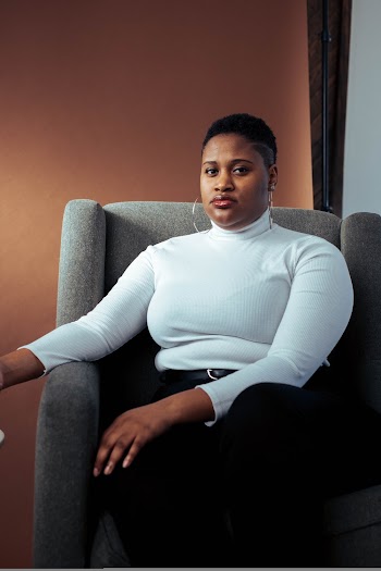 Woman in White High-neck Long-sleeved Top and Black Pants Sitting on Gray Fabric Sofa Chair
