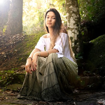 Woman In White Off Shoulder Top And Green Skirt Sitting In Middle Of The Woods 