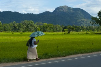 Woman in White Skirt Walking Along Road Holding Teal Umbrella
