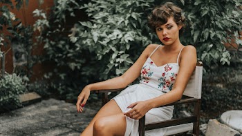 Woman In White Sleeveless Top And Shorts Sitting On Chair Near Green Outdoor Plants