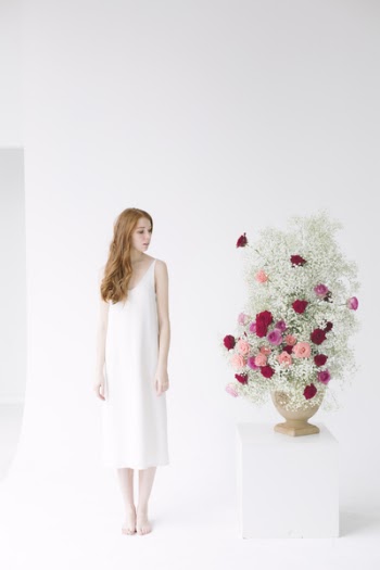 Woman in White Spaghetti Strap Midi Dress Standing Beside Table With Flowers