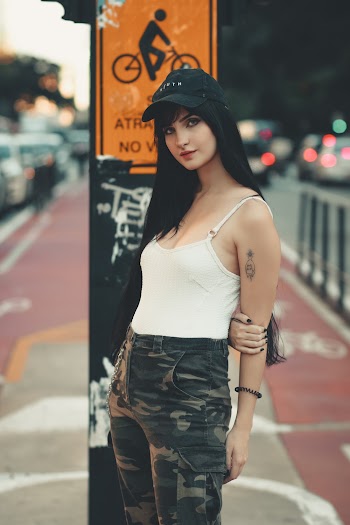 Woman In White Spaghetti Strap Top And Camouflage Pants Standing In Front Of Post