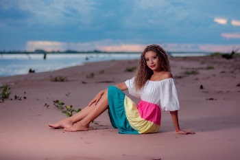 Woman in White Tank Top and Colorful Skirt Sitting on Brown Sand