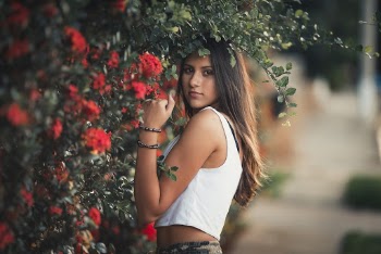 Woman in White Tank Top Standing Beside Red Flowers