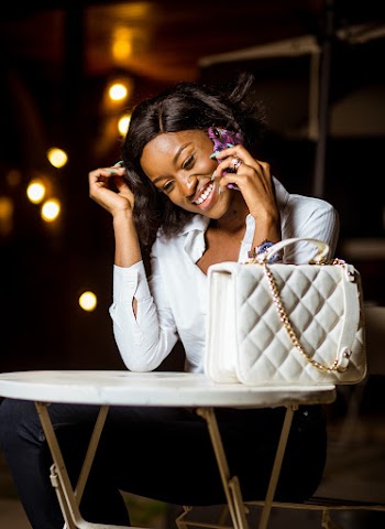 Woman in White Top and Black Pants Sitting Holding a cellphone 