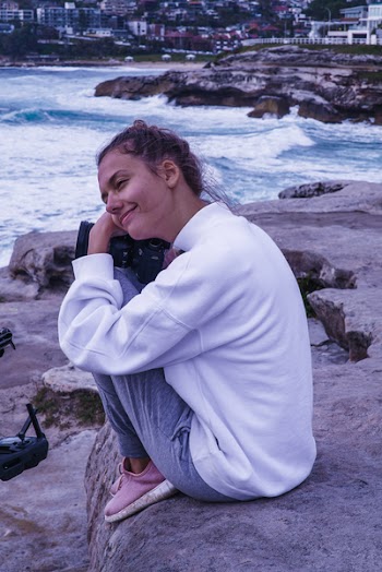 Woman in White Top and Gray Pants Sitting on Rock Formation