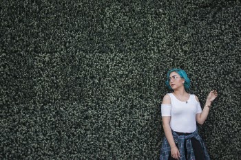 Woman in White Top Standing in Front of Green Leafed Hedge Wall