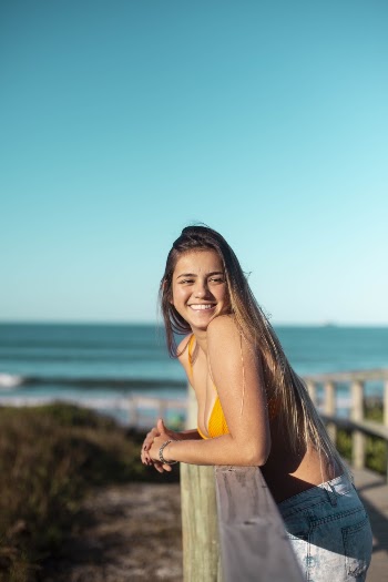 Woman in Yellow Bikini Smiling While Leaning on Wooden Rail