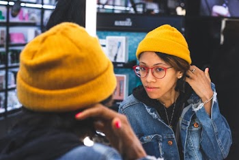 Woman in Yellow Bonnet, Red Framed Eyeglasses, and Blue Denim Jacket Facing Mirror