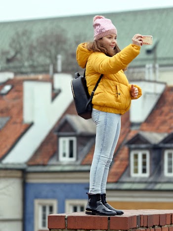 Woman in Yellow Puffer Jacket and Blue Jeans Holding Smartphone