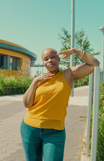 Woman in Yellow Sleeveless Top and Blue Jeans Leaning Left Hand on Fence
