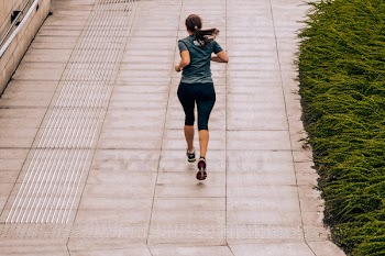 Woman Jogging on Grey Pavement Beside Lawn