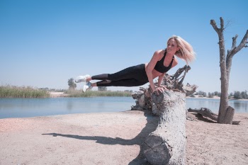Woman Jump on Tree Log Near Body of Water Under Blue Sky