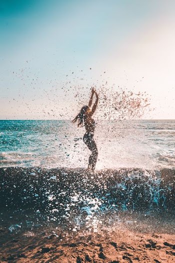woman jumping on seashore during daytime