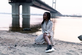 Woman Kneeling on Sand Near River and Bridge
