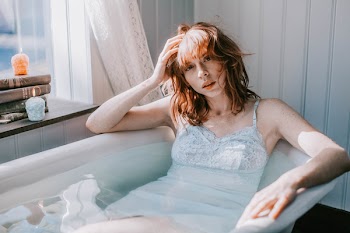 Woman Laying on Bath Tub While Holding Her Head