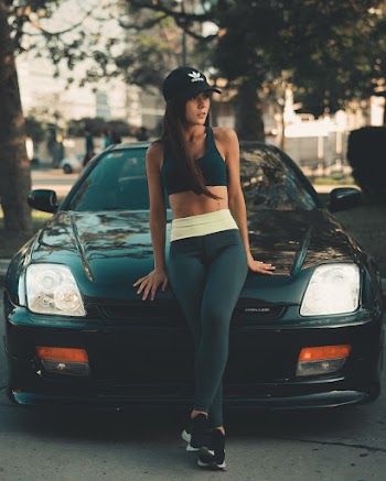 Woman Leaning On Black Car Wearing Black Cap And Sport Bra