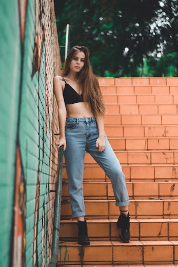 Woman Leaning on Brown Wall Wearing Black Brassiere and Denim Jeans